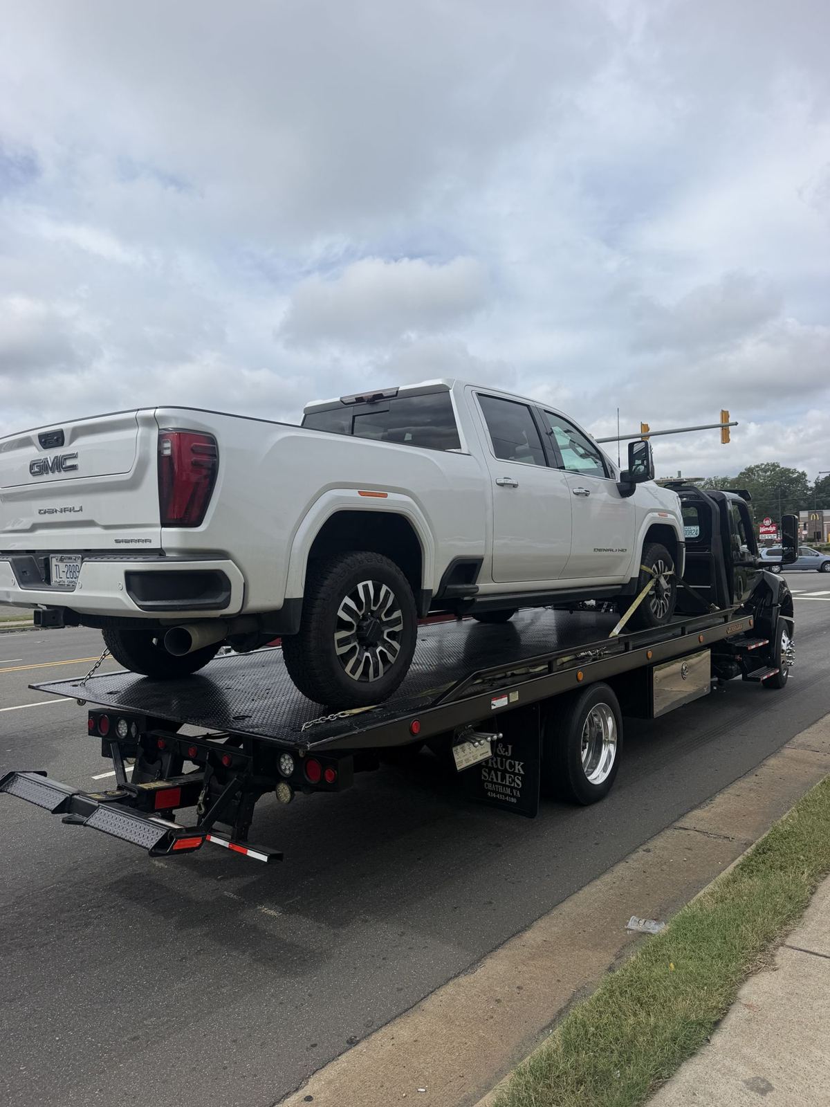 White GMC Sierra Denali HD secured on a flatbed tow truck on a Raleigh-Durham road