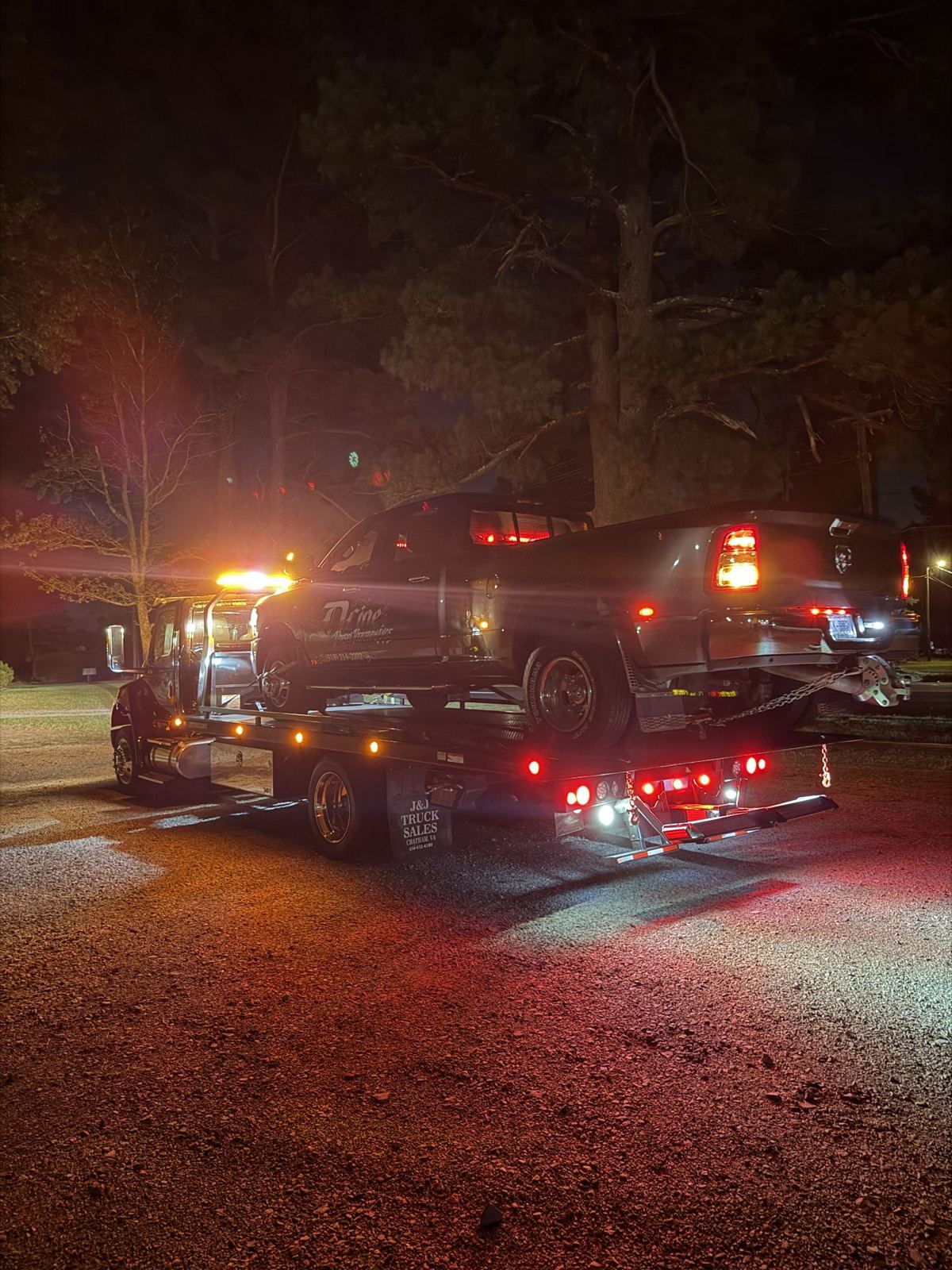 Rollback tow truck with amber lights on, towing a pickup at night