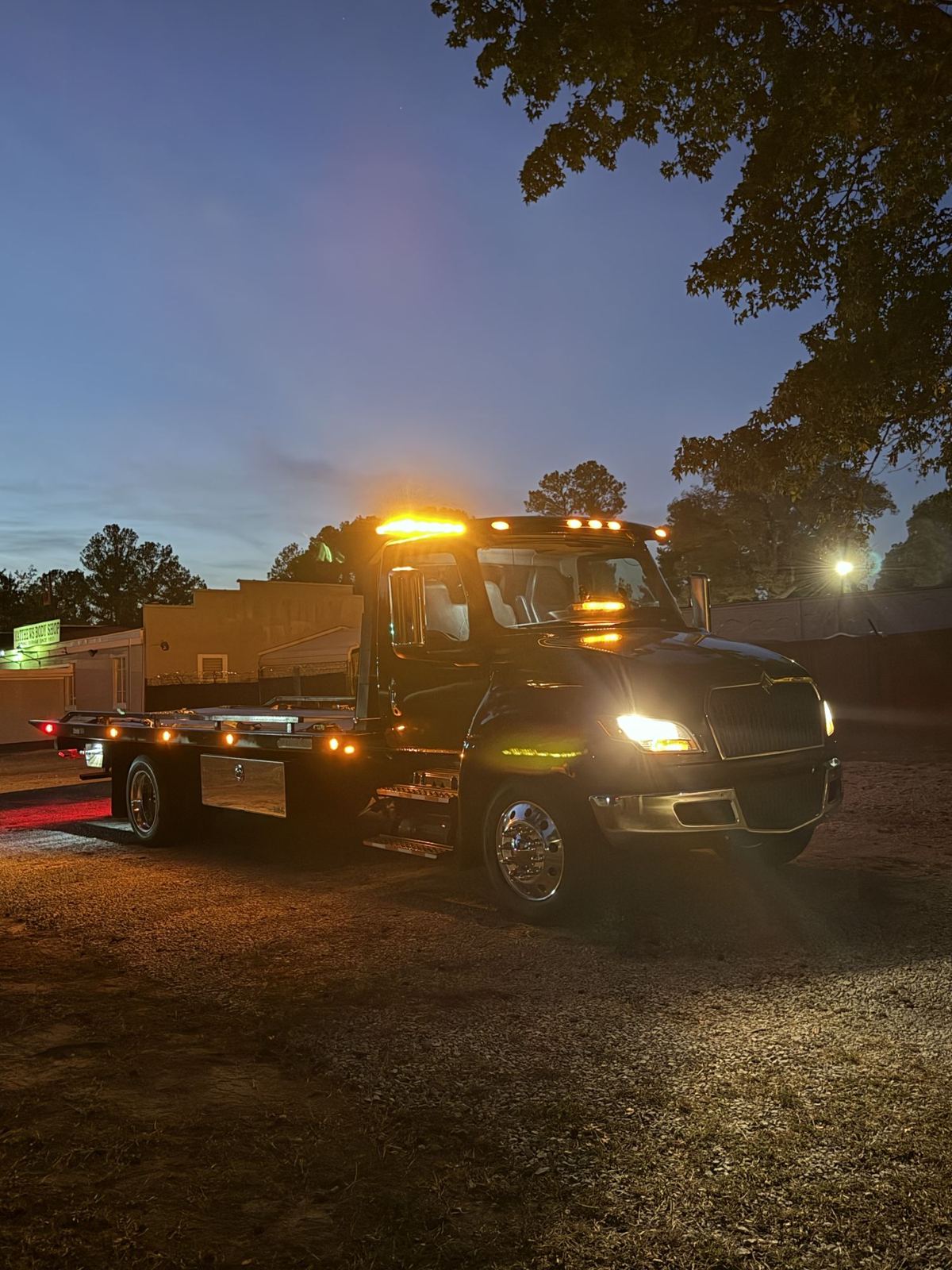 Ortma Towing's black International flatbed tow truck with amber lights on at dusk